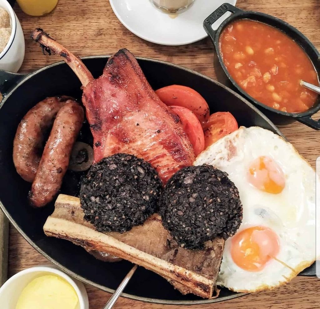 full english breakfast in a frying pan including sausages, eggs, bacon chop, bone marrow, black pudding and beans